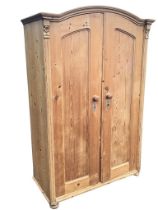 A European domed top pine wardrobe with cornice above panelled doors enclosing hanging space with