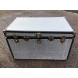 A large travel trunk with embossed aluminium panels framed by studded borders, with carrying handles