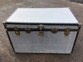 A large travel trunk with embossed aluminium panels framed by studded borders, with carrying handles