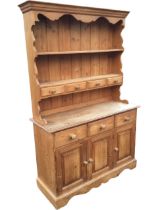 A pine dresser with moulded cornice and shaped apron above two shelves, the lower fitted with four