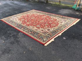 A Persian style carpet, the red field with allover floral decoration within conforming spandrels