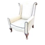 An Edwardian upholstered wing armchair, the arched back and outscrolled wings above a bowfronted