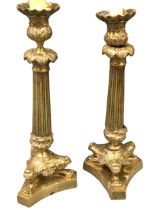 A pair of nineteenth century regency candlesticks with rippled trays on leaf cast urns above