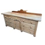 Antique pine dresser base with seven drawers about the recessed cupboard on bun feet, 181w x 55d x 9