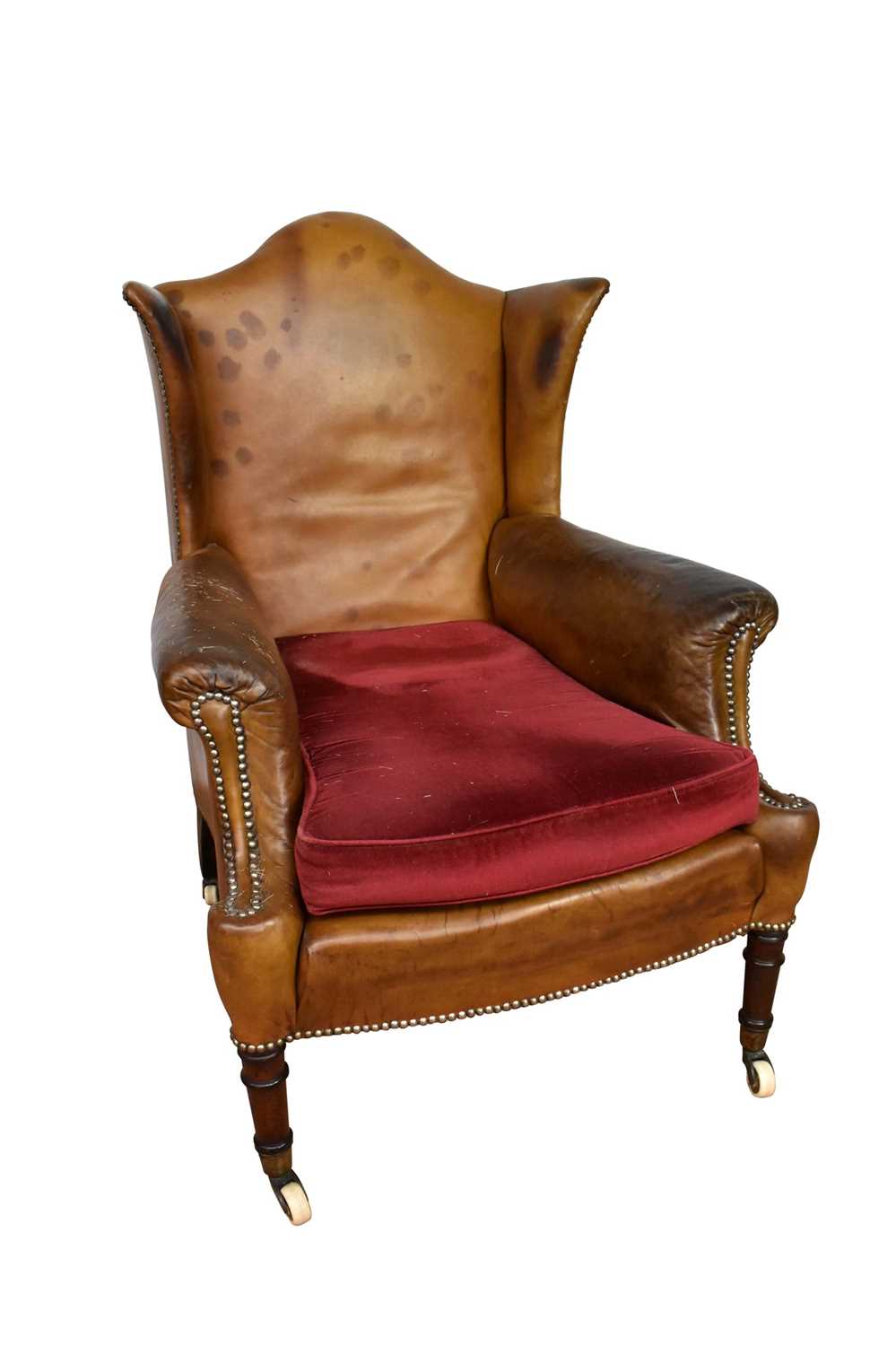 Early 19th century leather upholstered wing armchair, raised on ring turned legs and castors