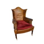 Early 19th century leather upholstered wing armchair, raised on ring turned legs and castors
