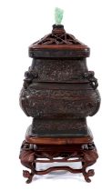 Antique Chinese bronze pot with a later carved wooden lid with jade finial, on a carved wooden stand