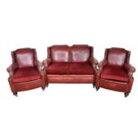 1920s stud closed red leather upholstery three piece suite, each of wing form, raised on bun feet an