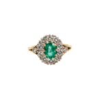 Emerald and diamond cluster ring with an oval mixed cut emerald measuring approximately 7.4 x 4.9mm,