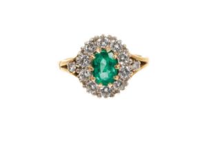 Emerald and diamond cluster ring with an oval mixed cut emerald measuring approximately 7.4 x 4.9mm,