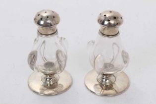 Pair of Edwardian Art Nouveau silver and glass pepperettes, (Birmingham 1906), each 6.5cm in height.