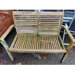 A teak two seater garden bench with slatted seat and back and shaped arms