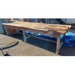 A large 3.48m long old pine and mixed wood work bench with plank top, set on three pairs of