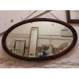 An early 20th Century stained oak bevelled oval wall mirror with carved detail to border