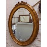 A reproduction gilt framed bevelled oval wall mirror with bow pediment and decorative border