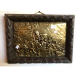 An embossed brass plaque depicting scenes of revelry, set in a heavy carved oak frame with