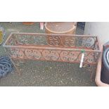 An ornate wrought iron oblong planter with scroll sides, set on square legs