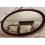 An early 20th Century stained oak bevelled oval wall mirror with carved detail to border