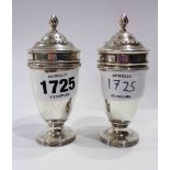 A pair of silver pedestal pepperettes with flambeau finials to push-fit lids - London 1933