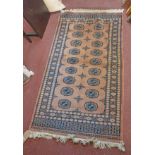 A handmade wool rug with two rows of Afghan repeat gul motifs within a wide border on old rose