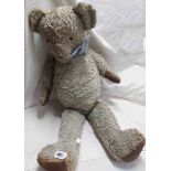 A large straw filled teddy bear with sewn leather paws