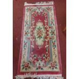 A Chinese washed wool rug with rose and swag decoration on a pink ground - 1.55m X 78cm