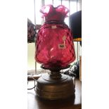 An old brass oil lamp with clear glass chimney and large cranberry glass shade