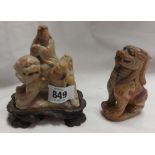 A Chinese carved soapstone figurine depicting scholars riding a lion set on carved hardwood