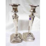 A pair of 25cm high silver candlesticks with tapered faceted stems and loaded stepped bases -