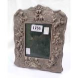 A silver fronted photograph frame with embossed cherub and vine decoration to border, with oak easel