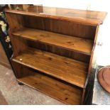 A 95cm modern stained pine three shelf open waterfall bookcase, set on bun feet