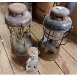 A box containing two vintage Tilly lamps and a small hurricane lamp