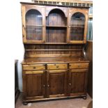 A 1.3m Ducal stained pine two part dresser with central open shelves and flanking glazed panel doors
