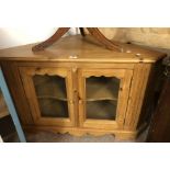 A 1.07m modern waxed pine corner cabinet enclosed by a pair of glazed panel doors, set on bracket