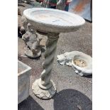 A cast concrete birdbath, set on an ornate twist column