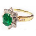 A marked 18k yellow metal ring, set with central oval emerald within an eight stone diamond border