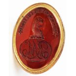 An antique rose metal ornate fob seal with device, initials and text banner to oval carnelian panel