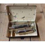 A vintage black japanned box containing a chrome plated syringe set