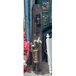 A vintage brass and iron water pump, set on a wooden backboard with mounting hook