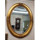 A reproduction ornate gilt framed bevelled oval wall mirror with decorative antique style border