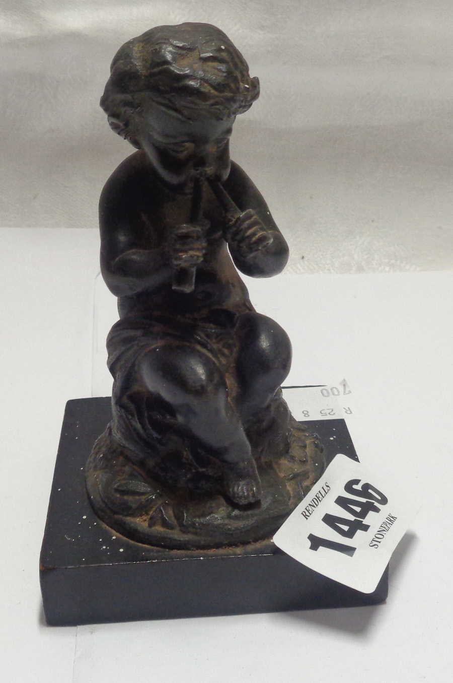 A small spelter figure depicting a child playing the pipes with antique finish, set on ebonised wood