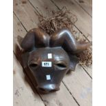 An African carved wood stylised Cape Buffalo mask with raffia to back and moving tongue