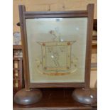 An antique oak framed fire screen with silkwork armorial under glass panel, set on massive semi-