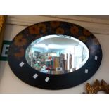 A 1920's ebonised framed bevelled oval wall mirror with painted floral decoration to top