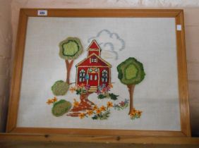 A vintage framed embroidered panel, depicting a building amidst trees