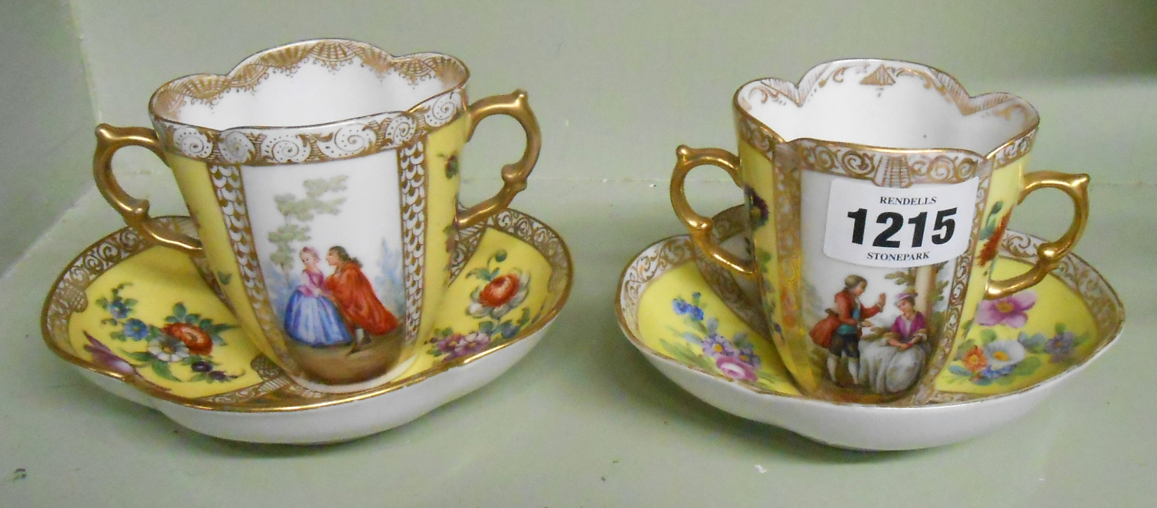 A pair of two handled Dresden porcelain cups and saucers each of lobed form with hand painted