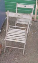 A pair of teak framed folding chairs with slatted backs and seats