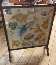 An early 20th Century stained wood framed fire screen with crewel style embroidered panel under