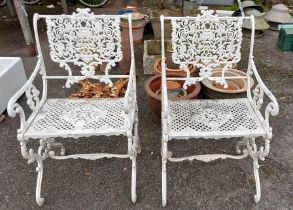 A pair of white painted cast aluminium garden elbow chairs with ornate pierced decoration in the