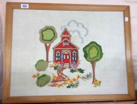 A vintage framed embroidered panel, depicting a building amidst trees